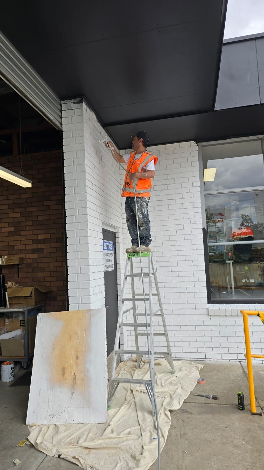 Painter on a ladder repainting a white brick commercial building