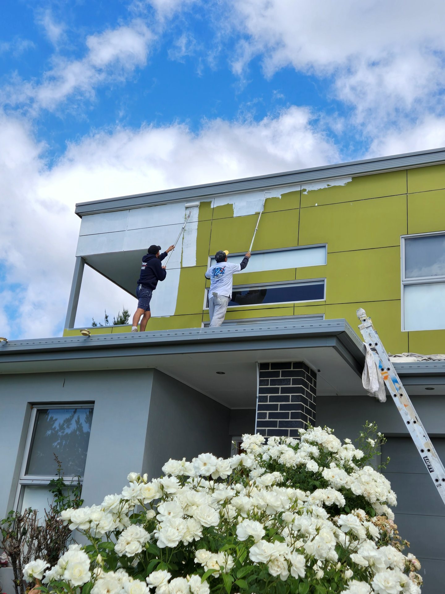 Painters on ladders repainting a two-storey home in a bold chartreuse green