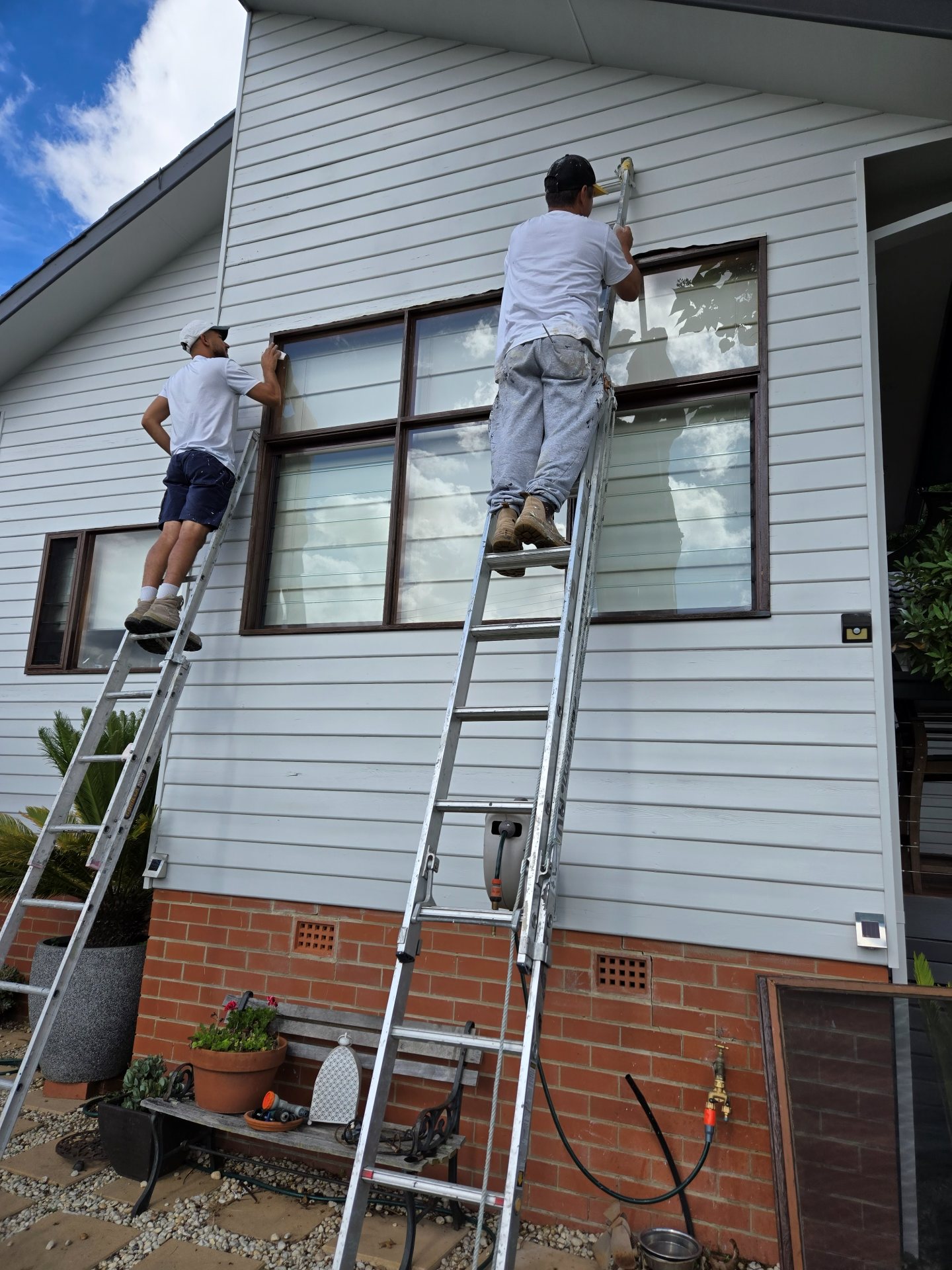 Two painters on extension ladders repainting a weatherboard home