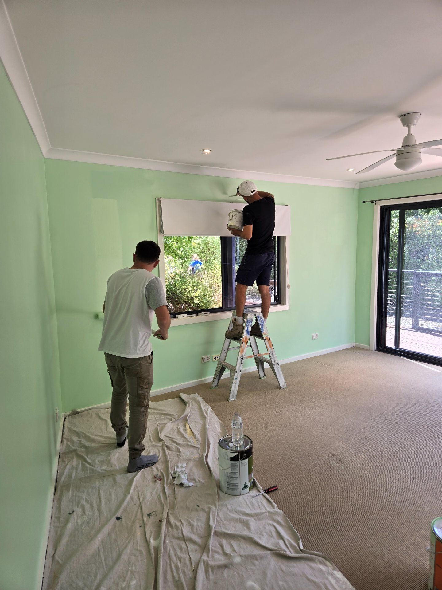 Painters installing a roller blind after repainting a mint-green bedroom